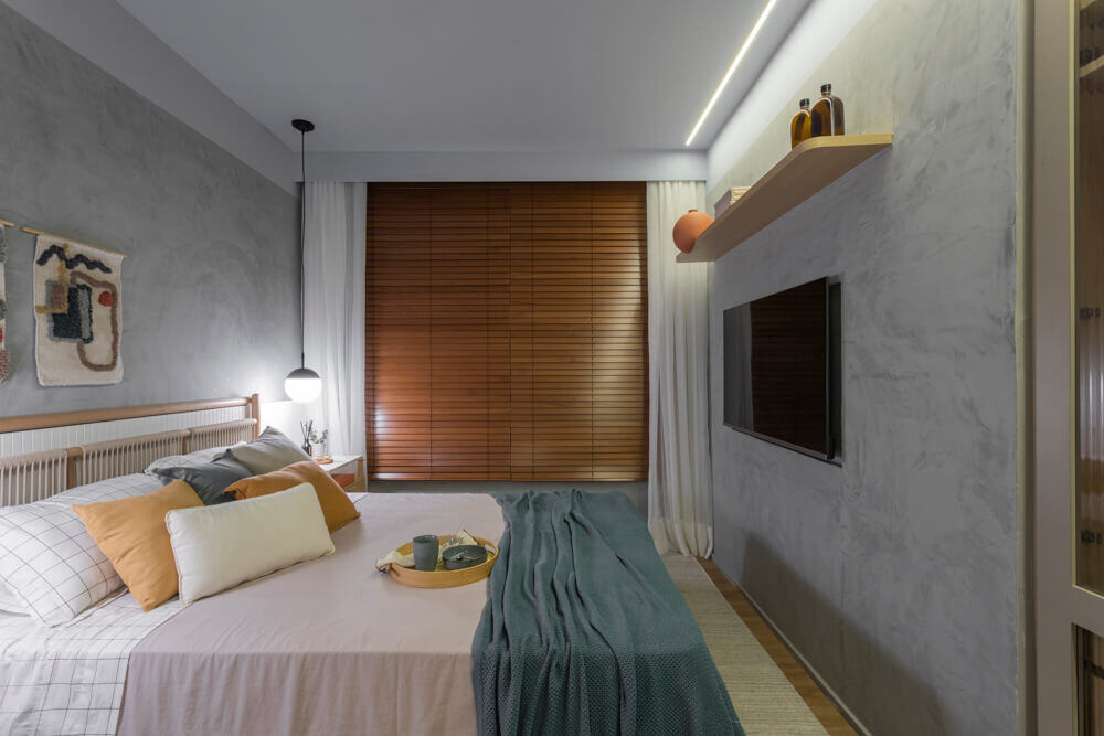 Quarto com uma cama de casal, prateleira de madeira na parede e iluminação no teto e pendentea