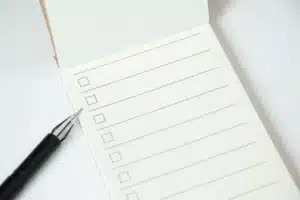 A imagem mostra um bloco de notas com uma lista de verificação (checklist) em branco e uma caneta.