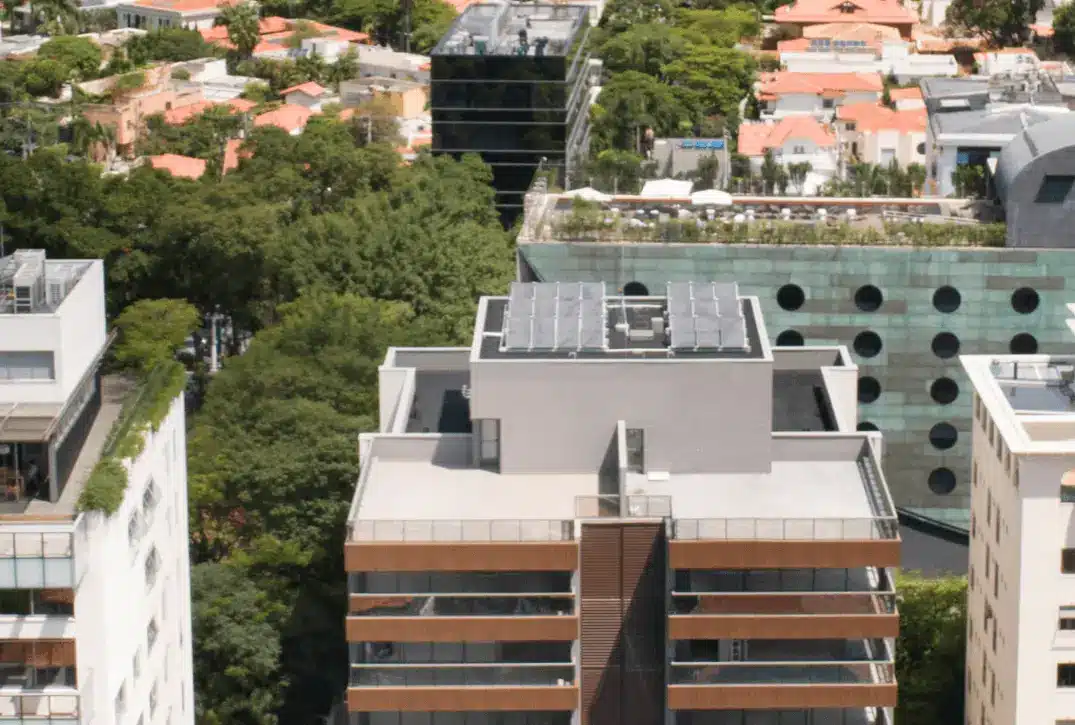 A imagem mostra uma vista aérea de edifícios residenciais e comerciais em uma área urbana densamente arborizada