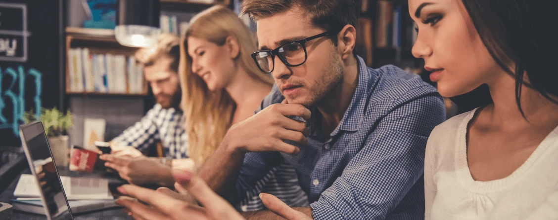 A imagem mostra um grupo de jovens adultos trabalhando ou estudando juntos em um ambiente que se assemelha a um escritório moderno ou biblioteca.